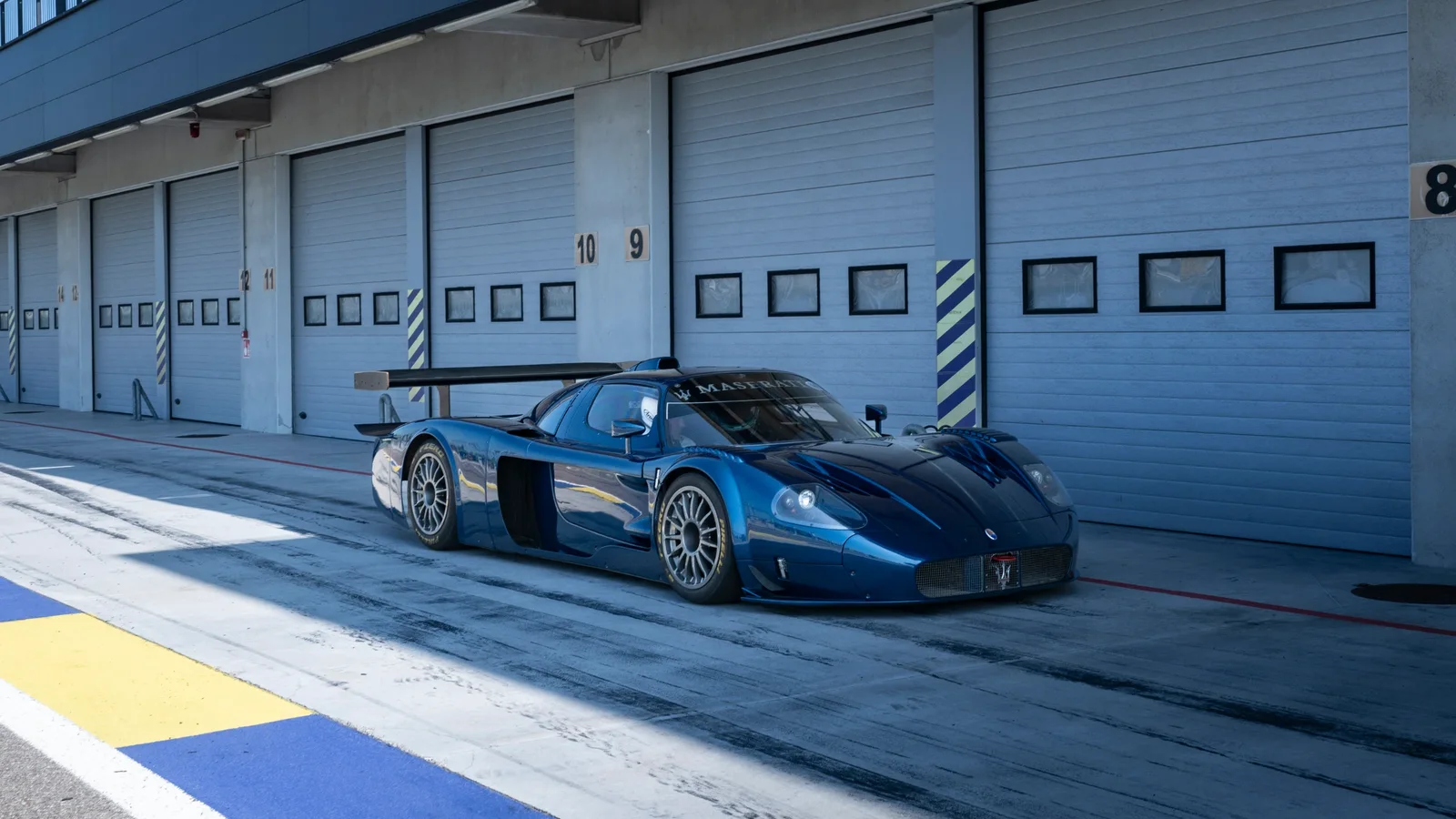Maserati MC12 albastru, pregătit în fața boxelor unui circuit.