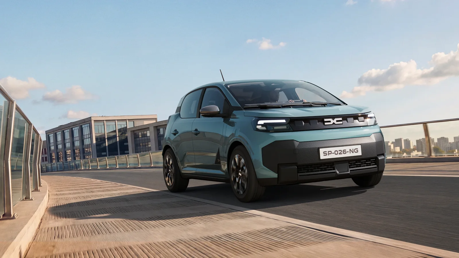 Noua Dacia Spring electrică, de culoare verde, surprinsă în mers într-un decor urban.