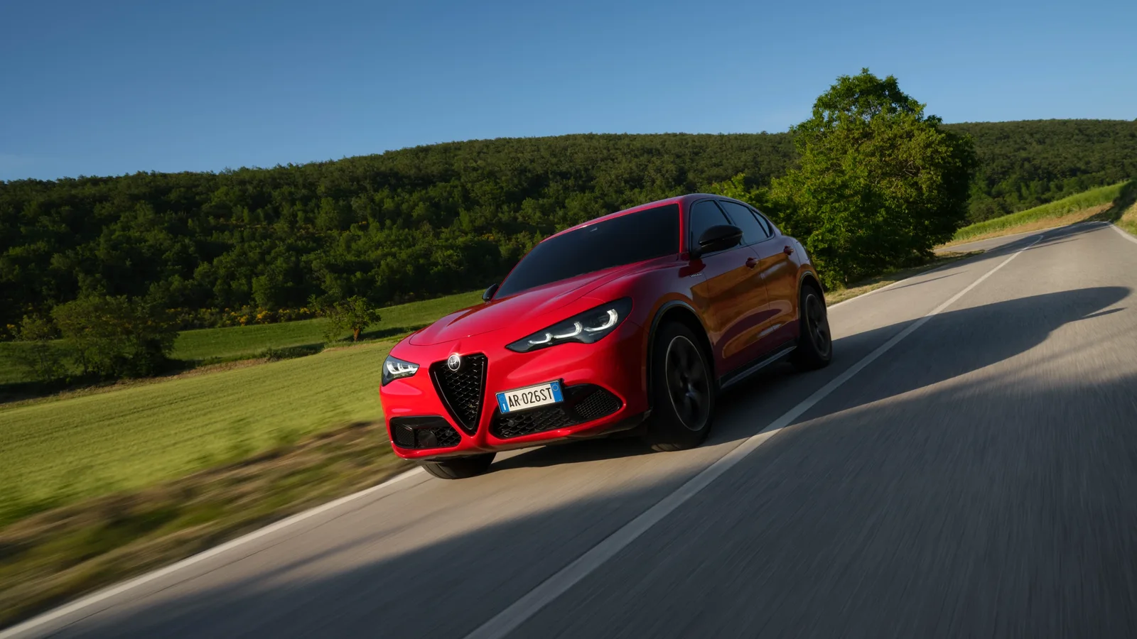 Alfa Romeo Stelvio roșu rulând pe un drum de țară, cu dealuri împădurite în fundal