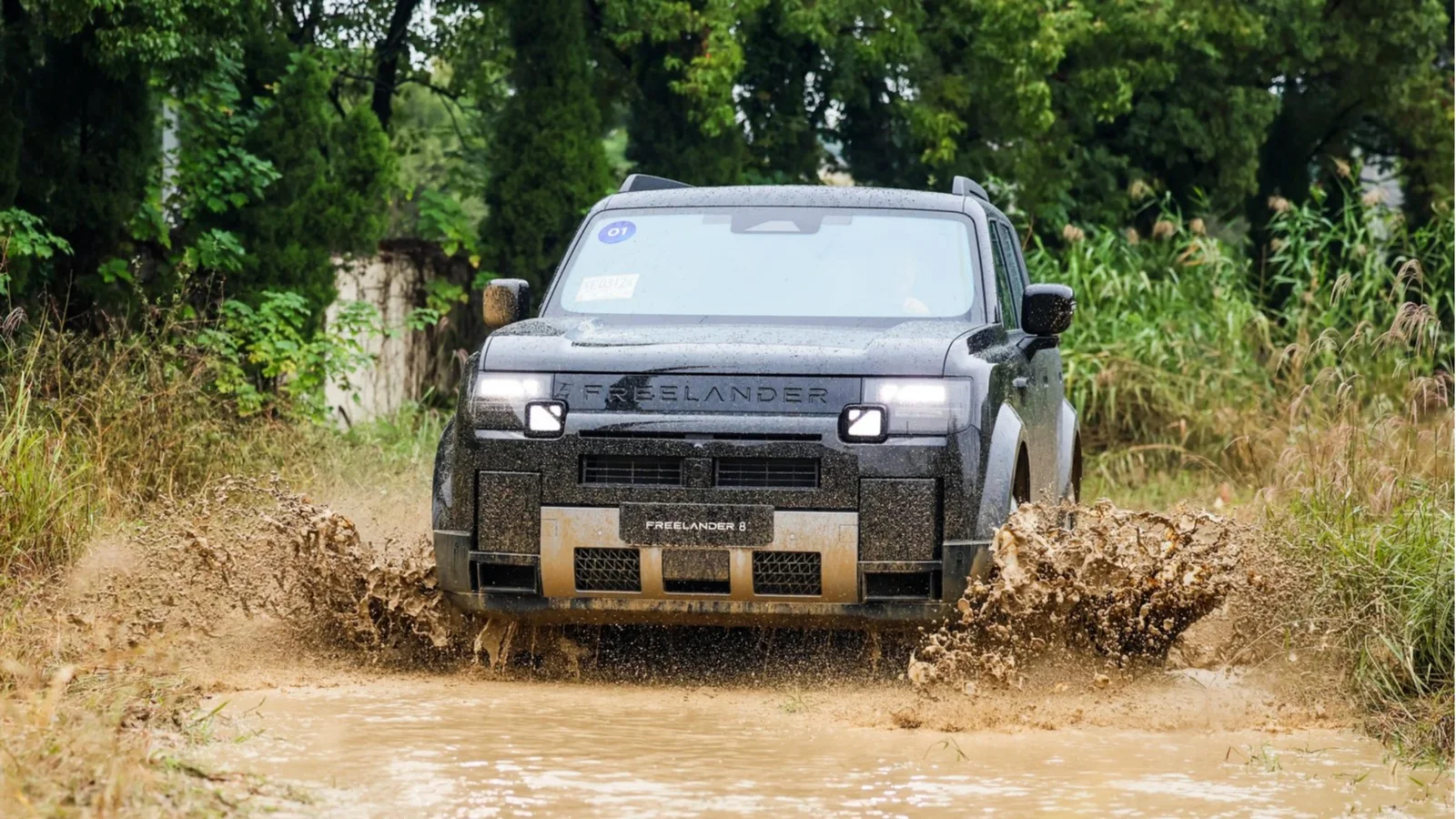 SUV Chery Freelander 8 de culoare gri închis, surprins frontal, traversând un vad cu apă în timpul unei probe off-road. Vehiculul stropeste apă și noroi, iar fundalul este format din vegetație și copaci verzi, fotografia fiind realizată pe un traseu natural.