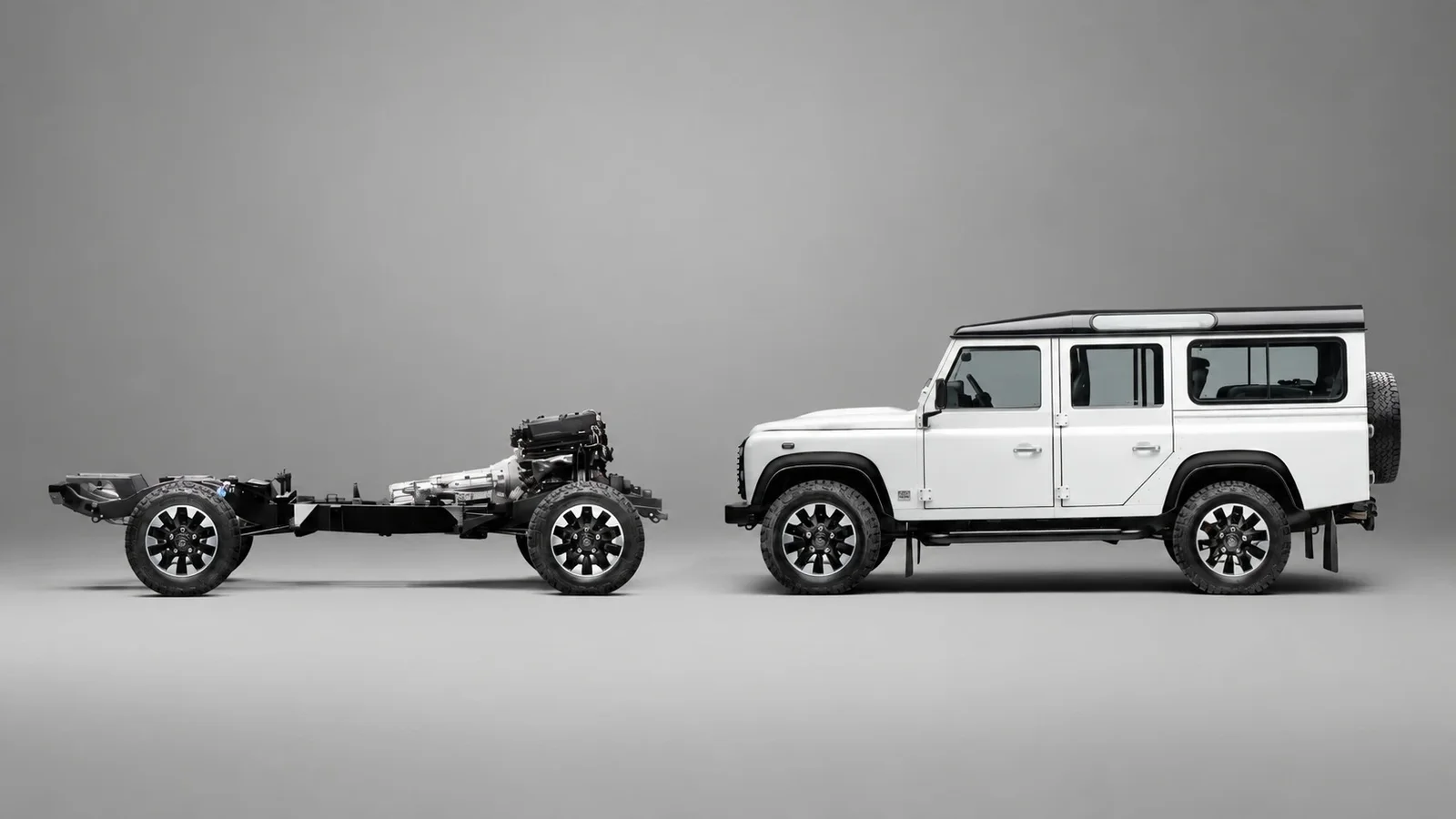 Defender clasic alb alături de șasiul separat, cu motor V8 și componentele mecanice expuse într-un studio