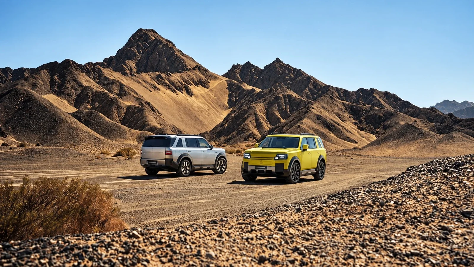 Două SUV-uri Freelander, unul argintiu și unul galben, pe un drum de pământ într-un peisaj montan arid