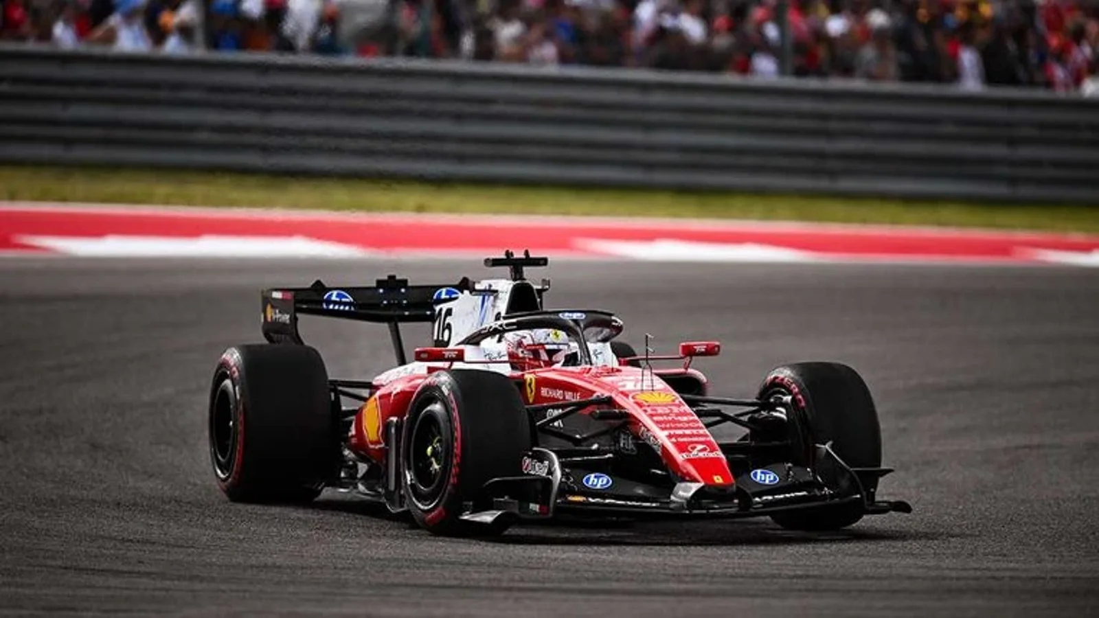 Formula 1 Ferrari SF-26 roșu și negru în viraj, fotografiat din față, pe Circuit of the Americas, șasiu în mișcare cu fundal neclar și spectatori în tribune.