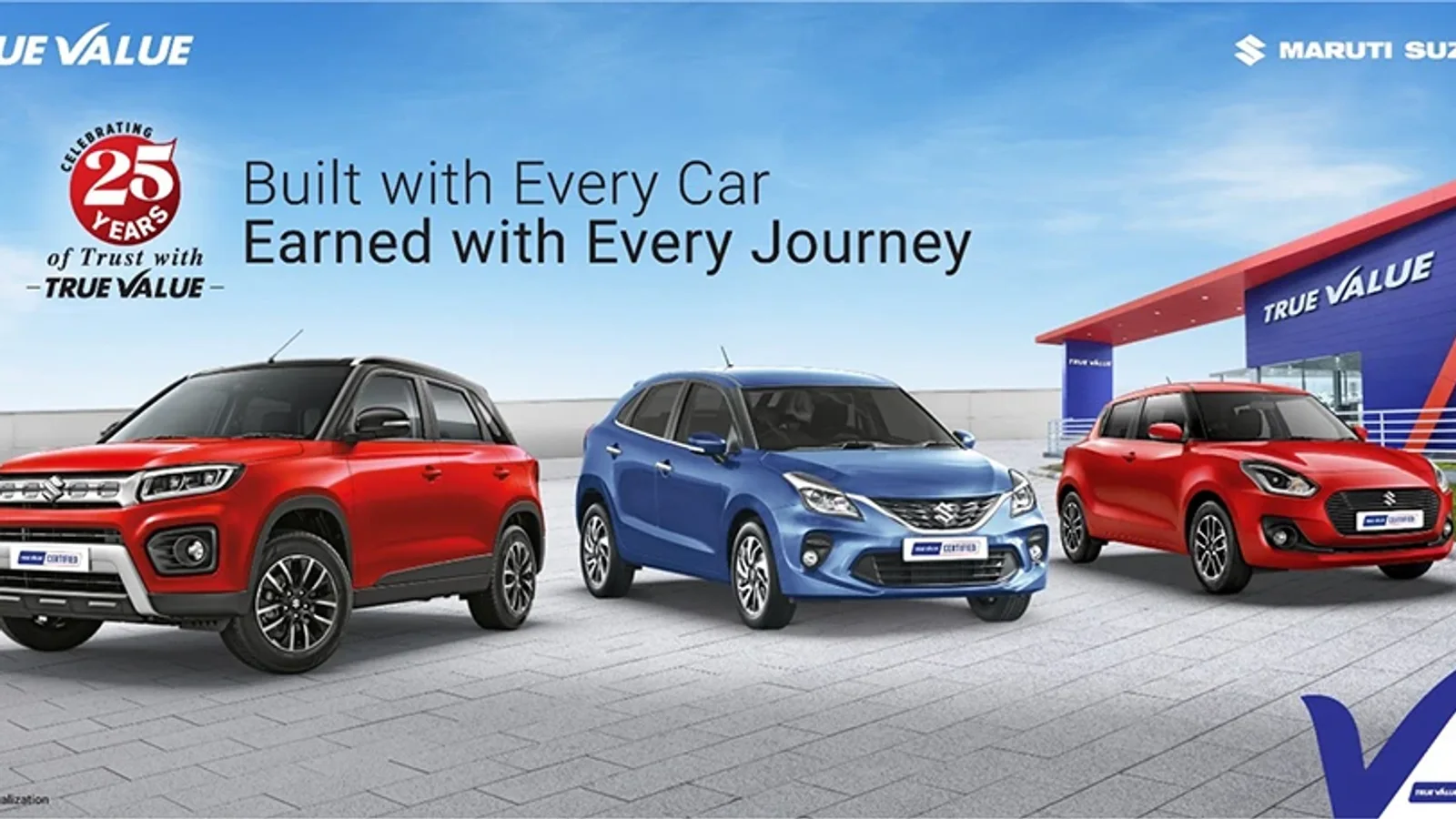 Trei mașini Maruti Suzuki True Value parcat în exterior lângă un stand de vânzări peste care se află un banner al programului. Trei SUV-uri și un hatchback în nuanțe de roșu și albastru, privite din vedere laterală și frontală. Fundal cu cer senin.