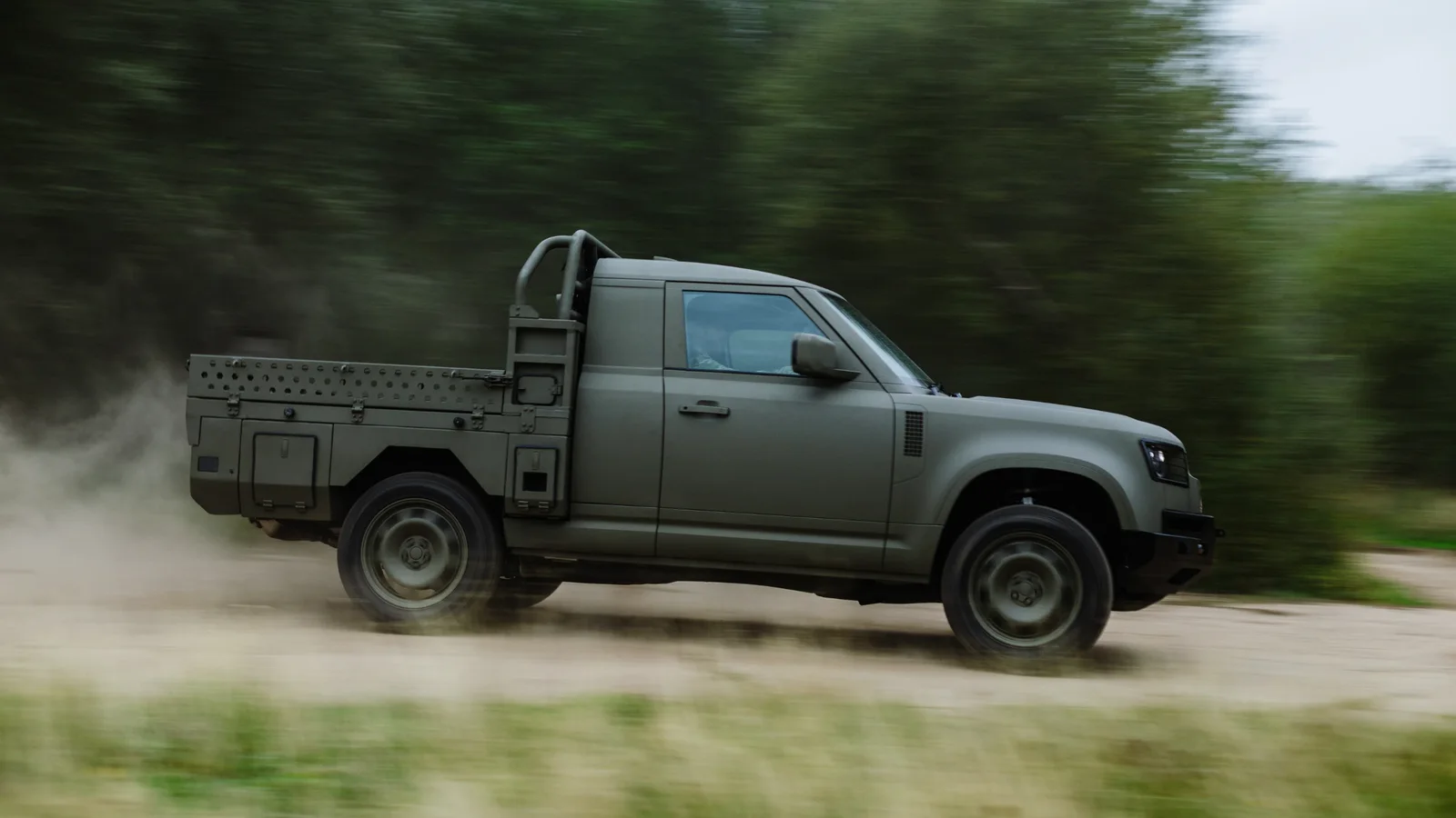 Defender Wolf Series II de culoare verde, în variantă pick-up, rulând pe un drum de pământ și ridicând praf.