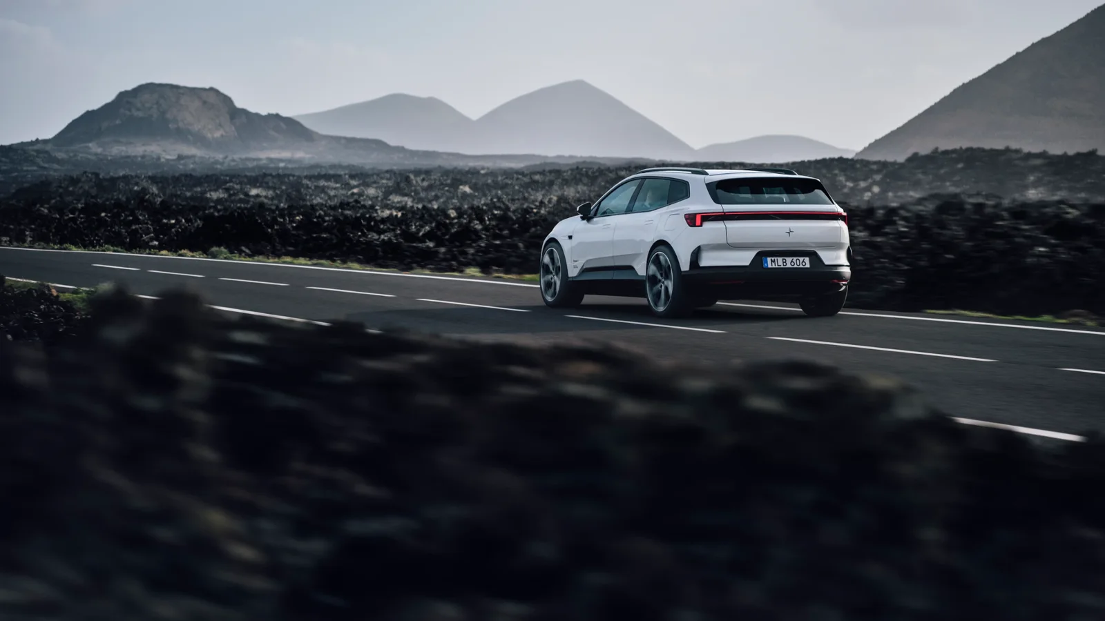 Polestar 4 alb, văzut din spate în timpul rulării pe un drum montan, într-un peisaj vulcanic.