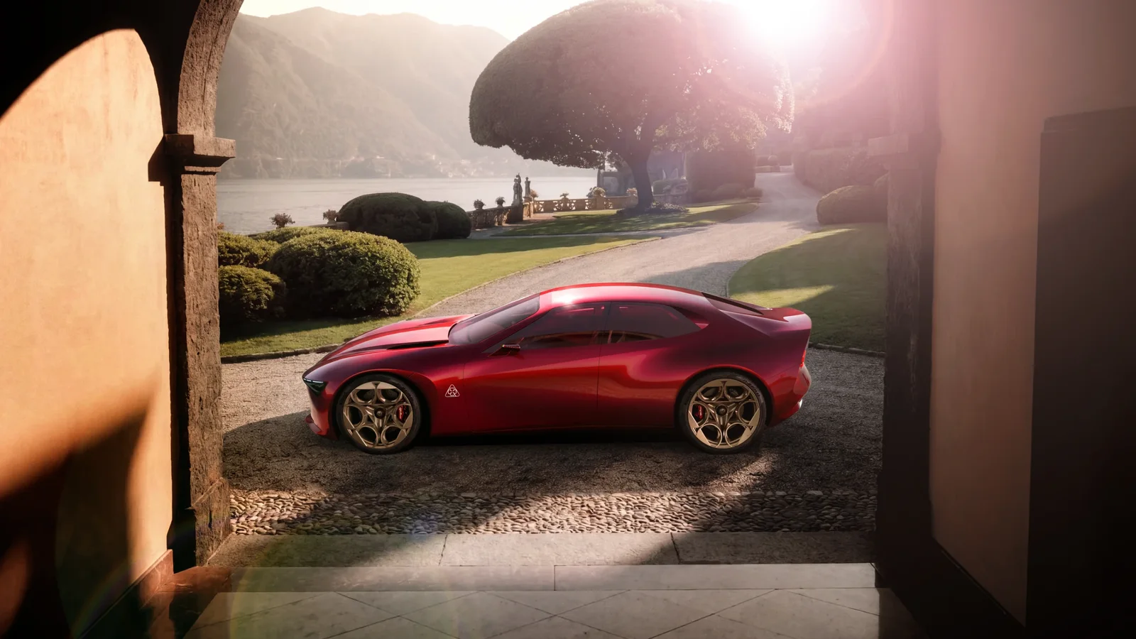 Alfa Romeo CuoreRosso roșu, fotografiat din lateral pe aleea unei vile, cu lacul și munții în fundal.