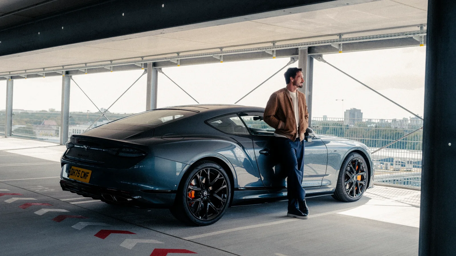 Bentley Continental GT albastru parcat într-o parcare etajată, lângă un bărbat sprijinit de automobil.