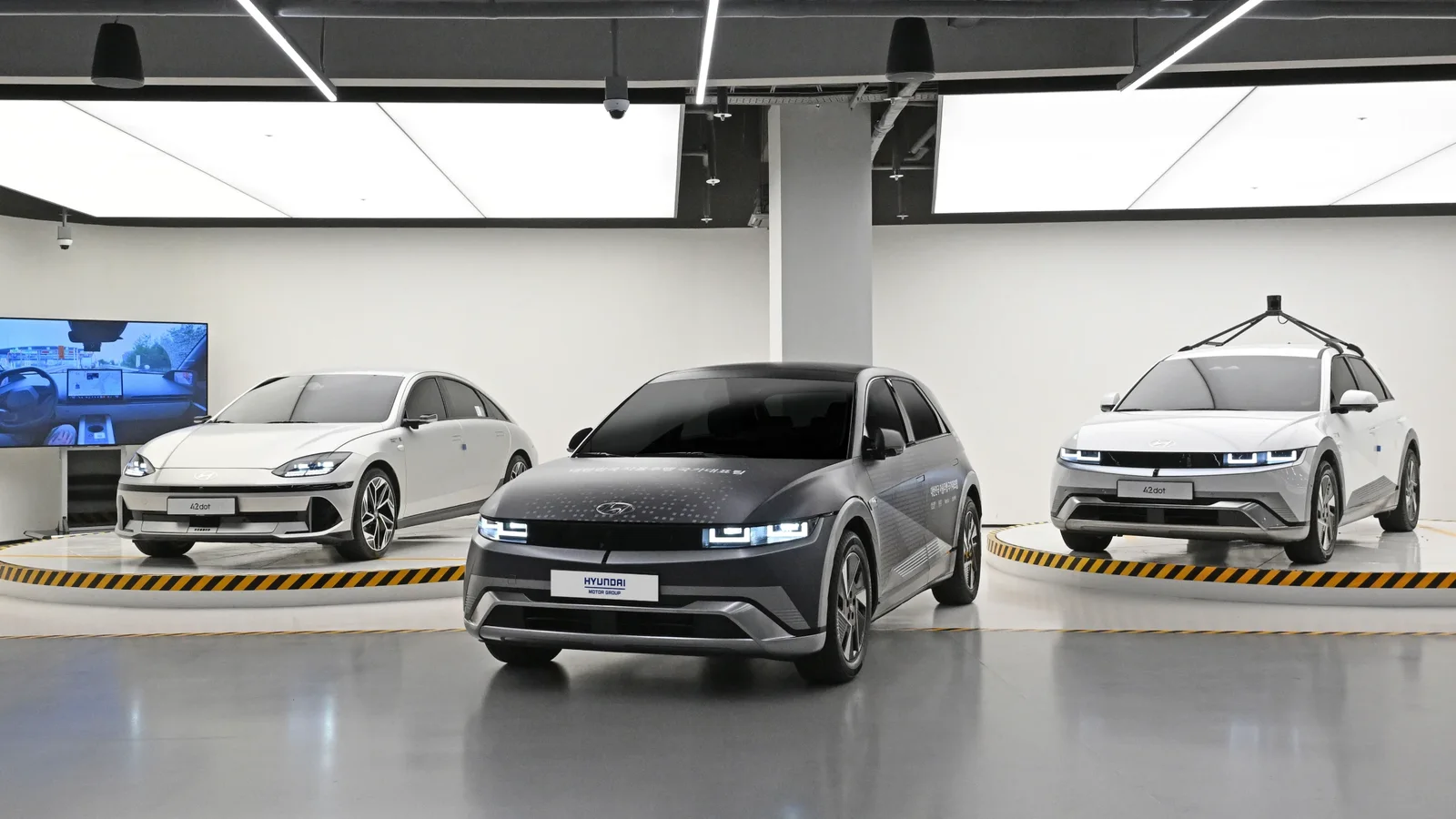 Trei automobile Hyundai într-un laborator de testare, inclusiv un SUV poziționat central și un vehicul echipat cu senzori pentru conducere autonomă.