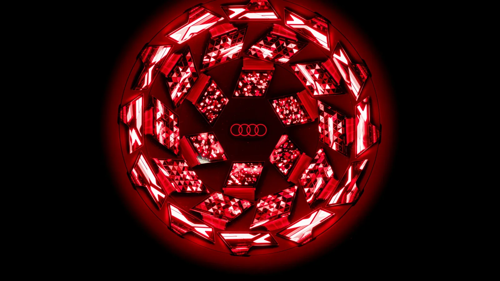 Detaliu macro al stopului OLED digital curbat de pe Audi Q9, iluminat în roșu intens pe fundal negru, evidențiind cele 512 segmente luminoase dispuse tridimensional în forma circulară a panoului.