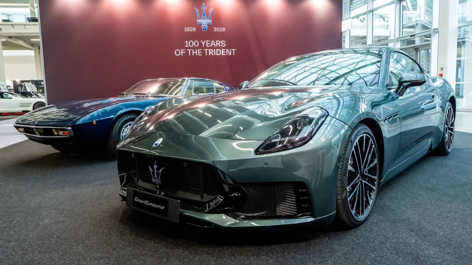 Două modele Maserati la standul Motor Valley din salonul Auto e Moto d’Epoca, Bologna: în prim-plan GranTurismo Trofeo Verde Giada, culoare verde metalizat, iar în fundal Ghibli SS Coupé din anii 1970, albastru închis, expuse sub un panou roșu cu text aniversar.