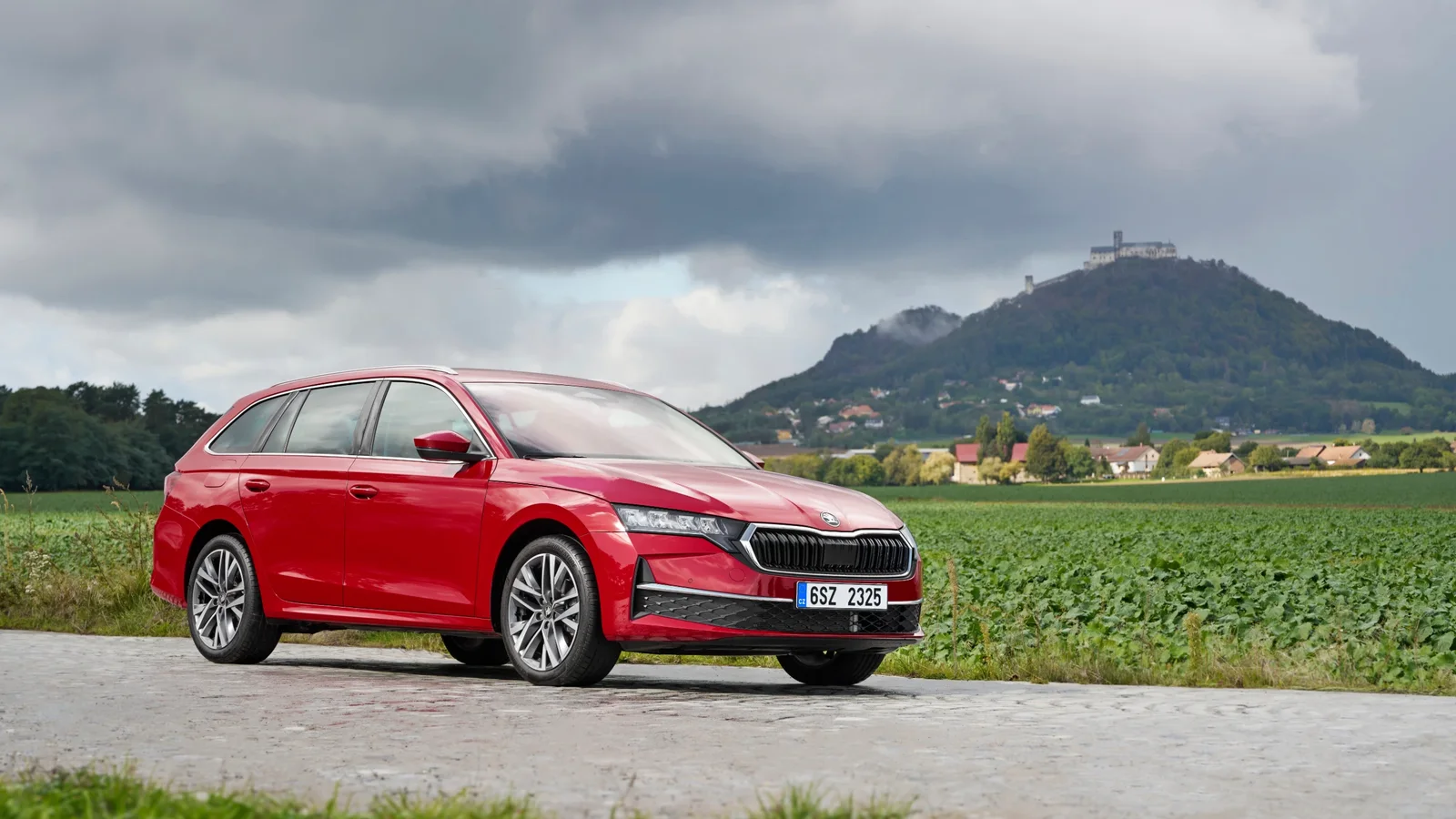 Škoda Octavia Combi roșie parcată pe un drum de țară, cu un deal și un castel în fundal