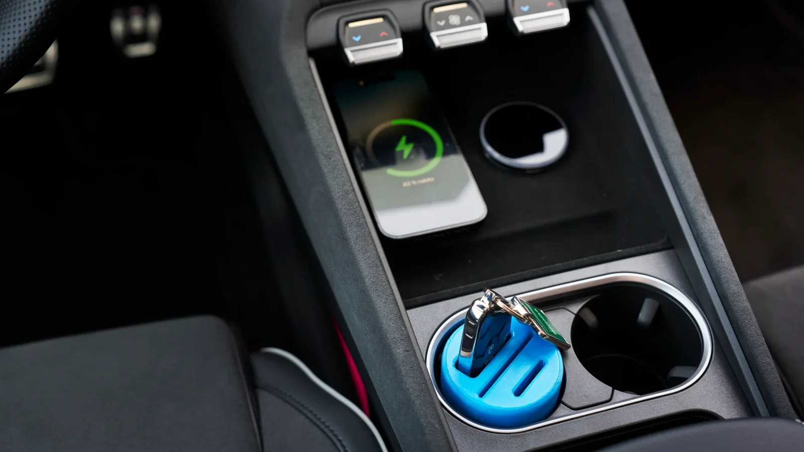 Interior de mașină Škoda, vedere asupra consolei centrale cu suporturi pentru pahare, unul dintre ele conținând un accesoriu albastru imprimat 3D, lângă comutatoare și întrerupătoare montate orizontal, tonuri negre și gri predominante.