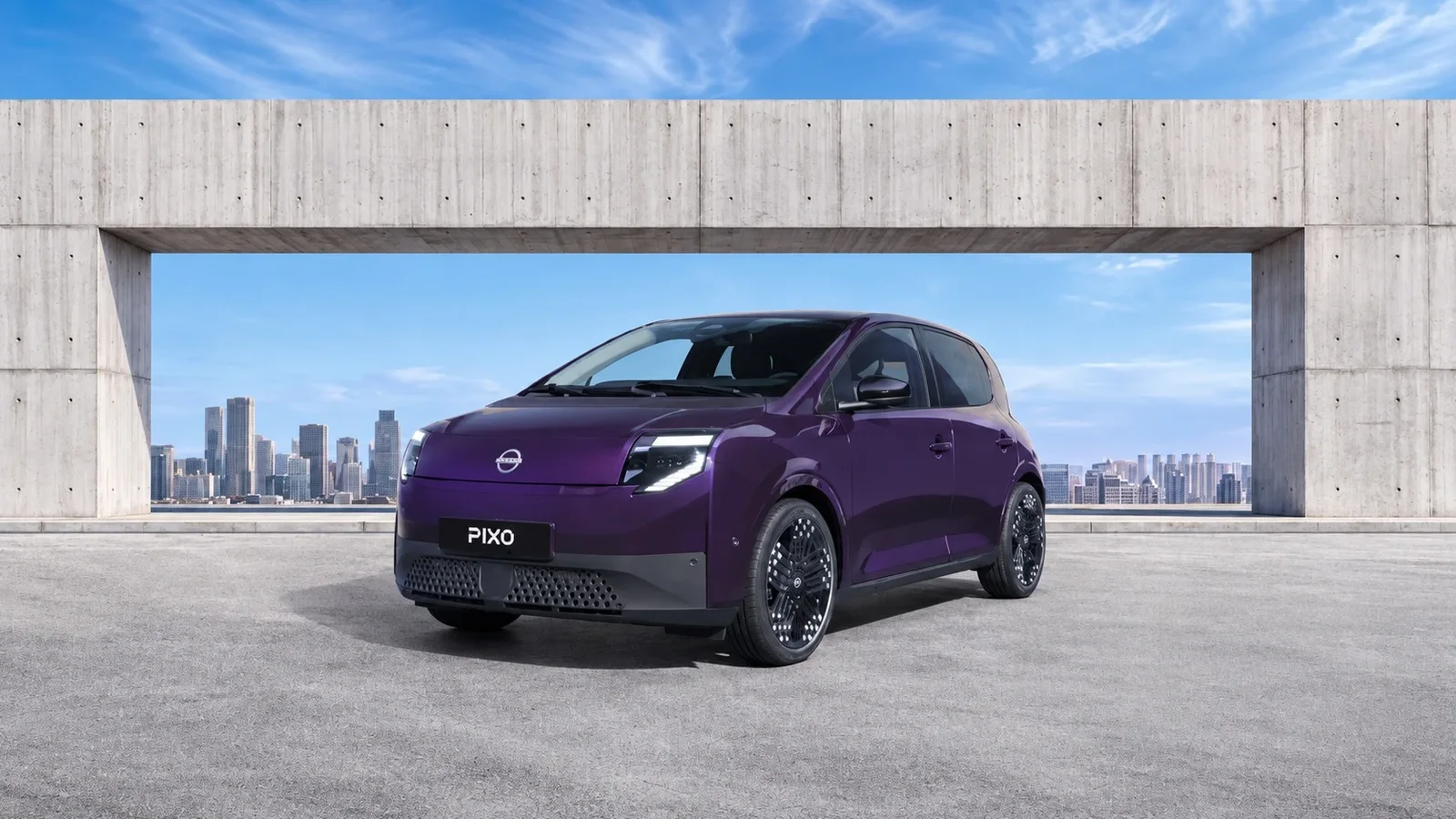 Nissan PIXO electric mov, fotografiat în fața unei structuri din beton, cu panorama orașului în fundal.
