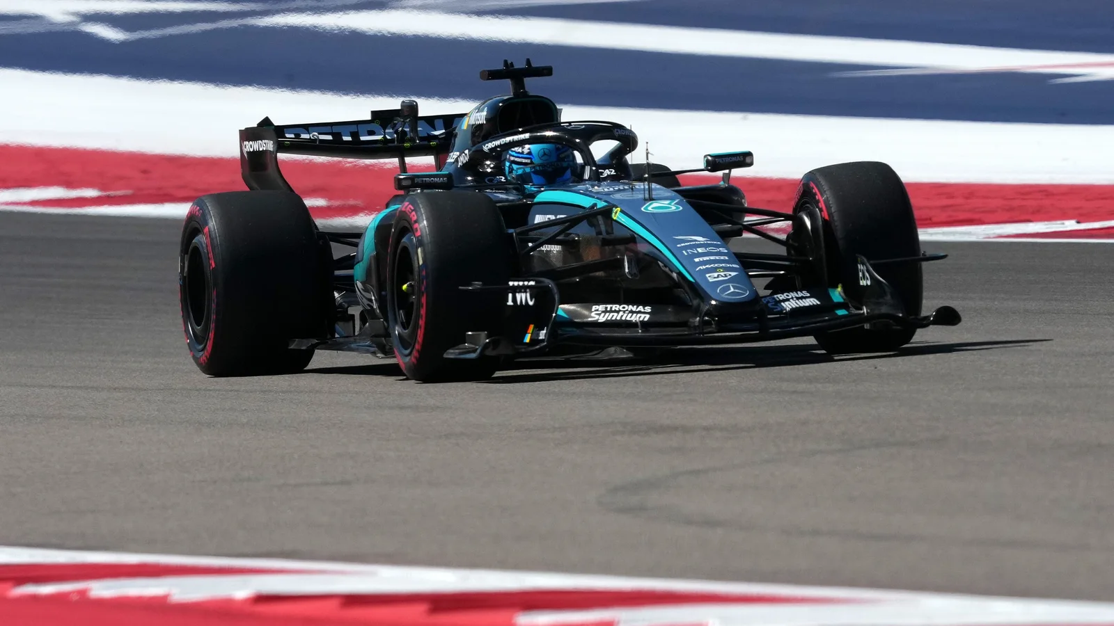 Monopost Mercedes W17 negru cu accente albastre, de Formula 1, pe circuitul de la Austin, surprins din față-dreapta, în timp ce trece peste o porțiune a pistei cu marcaje alb-roșii.