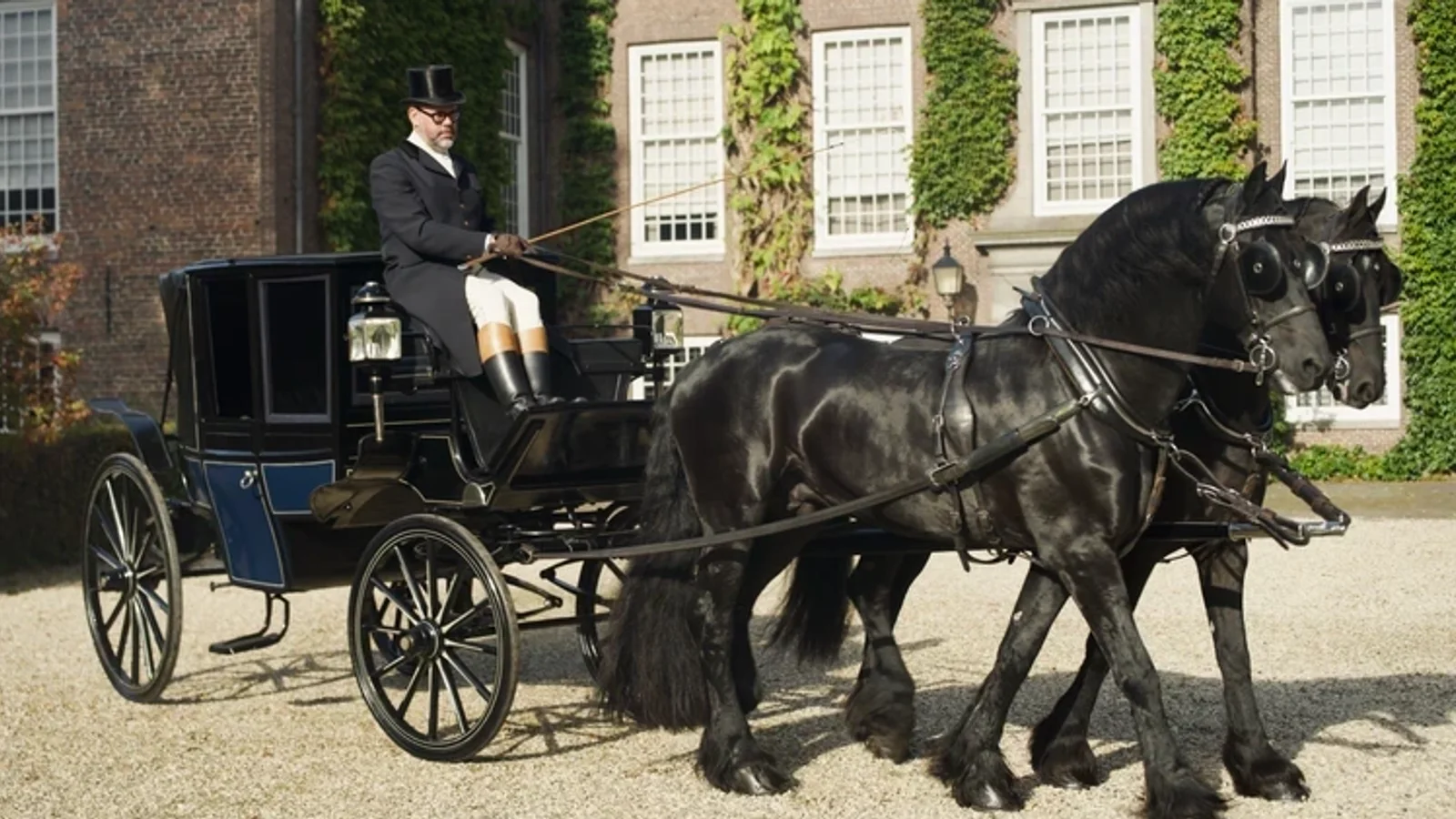 Trăsură Spyker Landauer din 1890, trasă de doi cai negri frizieni, fotografiată din lateral pe o curte cu pietriș în fața unui castel cu ferestre înalte și ziduri din cărămidă. Căruțaș îmbrăcat în costum negru și pălărie.
