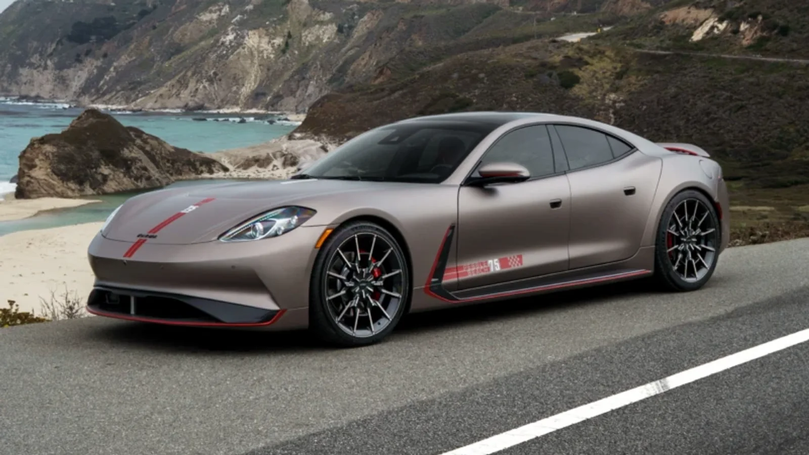 Automobil Karma Gyesera PB75, vopsit în nuanța Electrum Gold cu accente roșu Stellar, surprins lateral pe un drum de coastă, cu peisaj muntos și ocean în fundal, sub un cer senin. Jante de 22 inci și etriere roșii sunt vizibile.