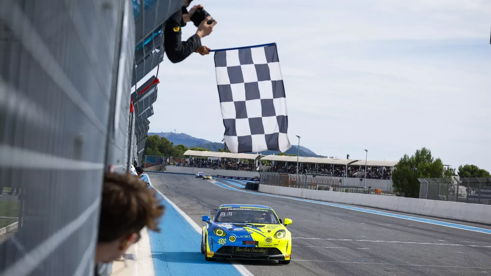 Alpine A110 Cup galbenă trece linia de sosire la Circuit Paul Ricard, în timp ce este fluturat steagul în carouri.