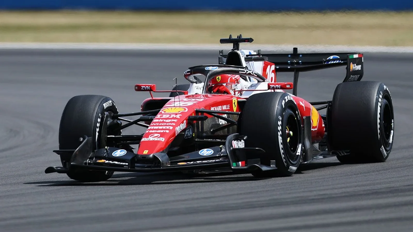 Monopost Ferrari de Formula 1, roșu cu detalii negre și albe, pe asfaltul unei piste în timpul unei curse, surprins din față-lateral dreapta. Mașina are aripile aerodinamice vizibile și pneuri slick. Fundal desfocalizat cu bariere de protecție.