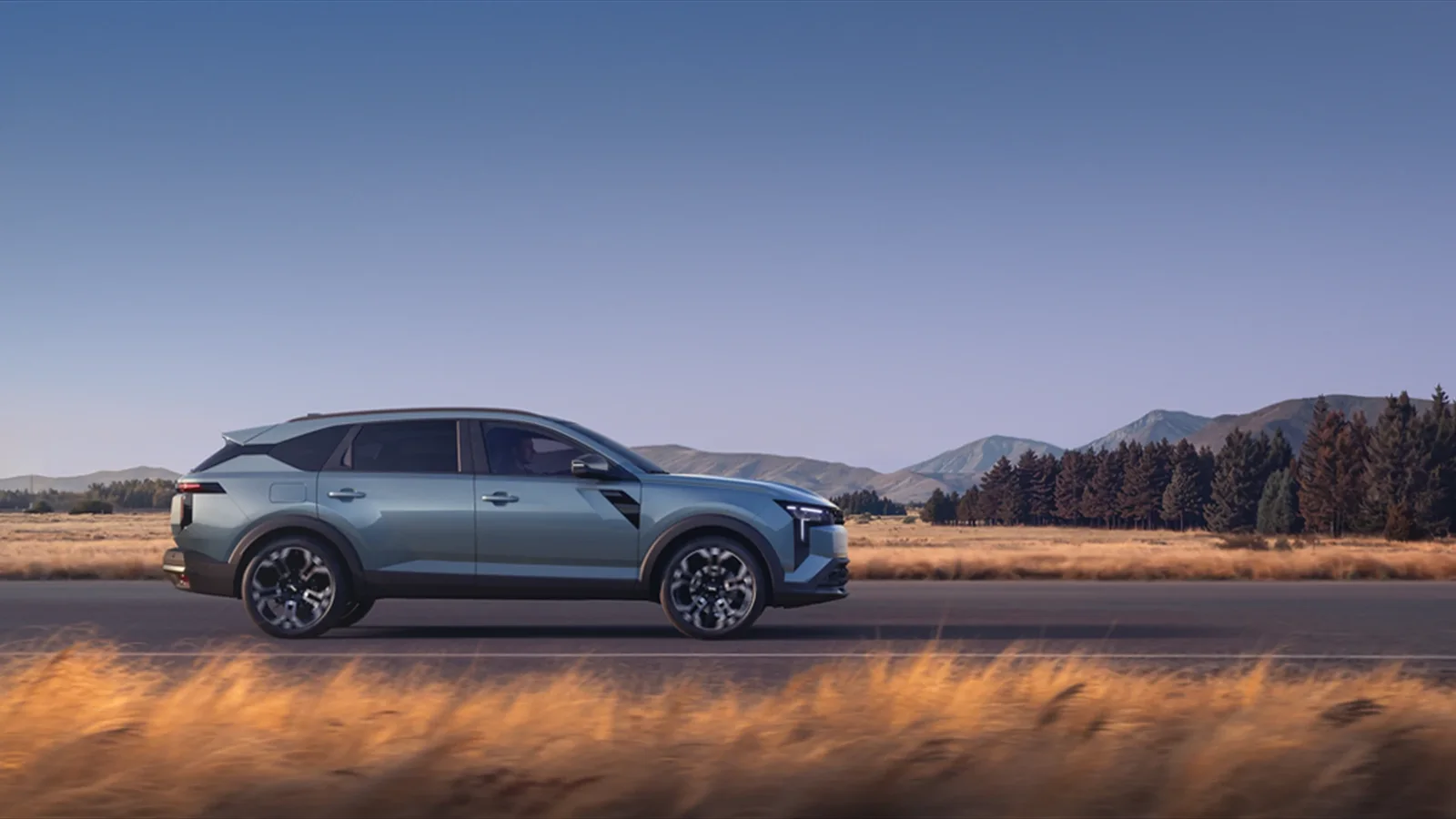 Dacia Striker albastru, văzut din profil pe un drum de munte, cu pădure și culmi în fundal.