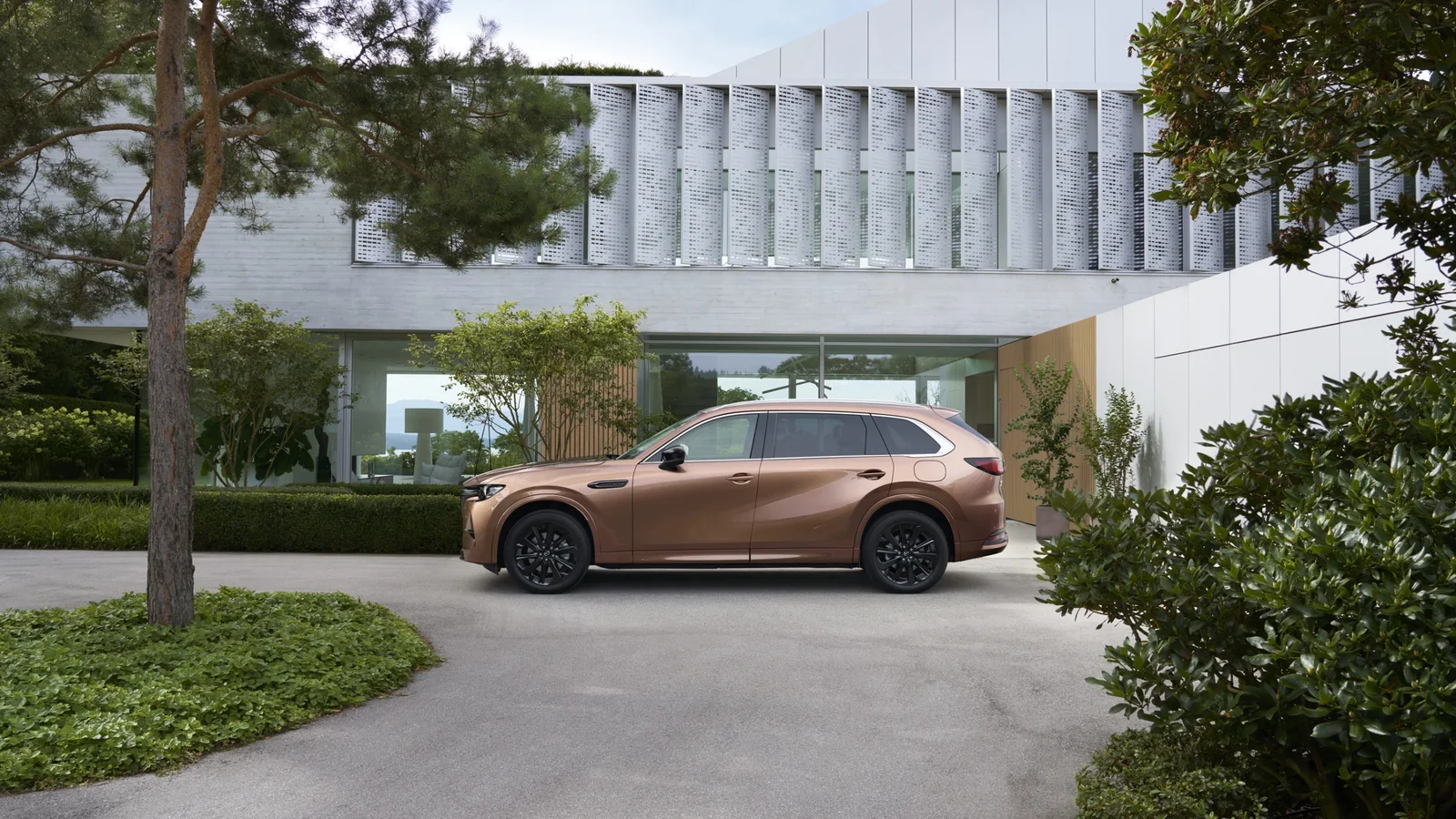 Mazda CX-80 parcat în fața unei locuințe moderne, înconjurată de vegetație.