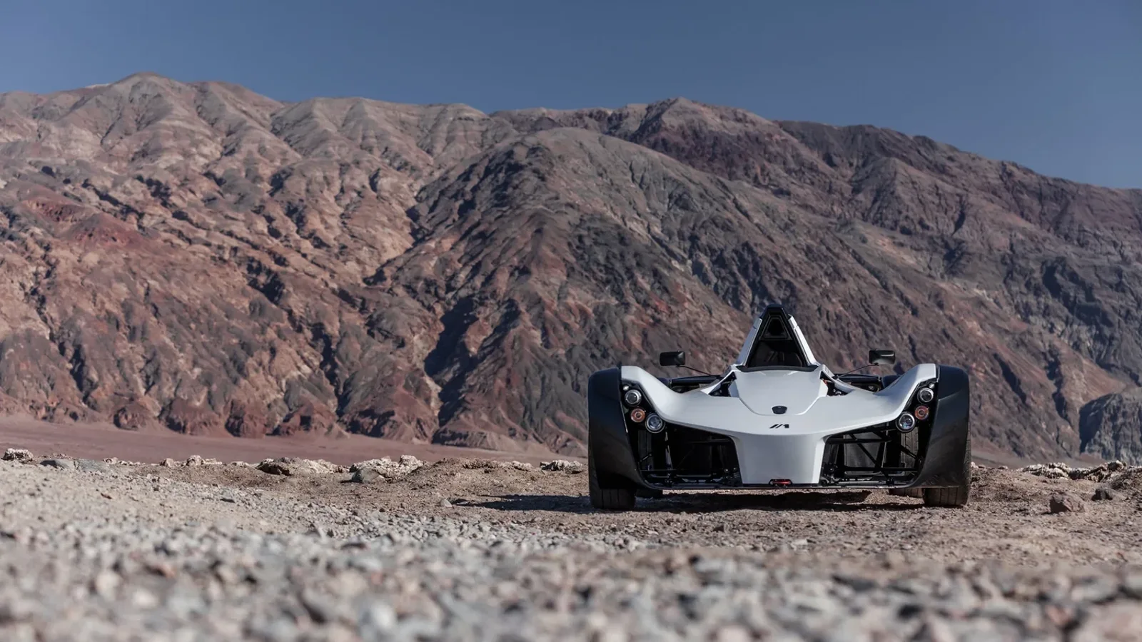 BAC Mono R alb, fotografiat frontal pe un teren stâncos, cu munți în fundal.