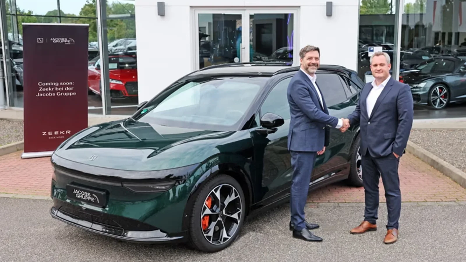 Doi reprezentanți Jacobs Gruppe dau mâna lângă un automobil electric Zeekr verde, în fața unui showroom.